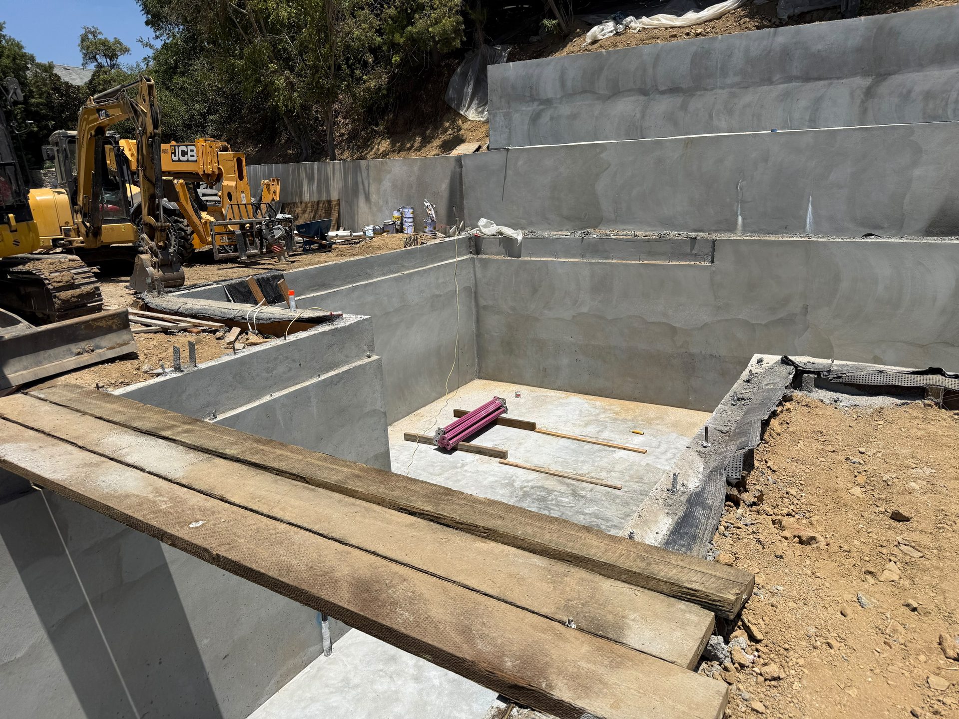 Excavator grading a hillside lot alongside new foundation walls
